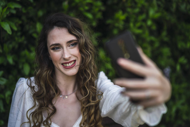 A shallow focus shot of a beautiful Spanish Caucasian woman wearing top and jeans, taking a selfie - Fotó, kép