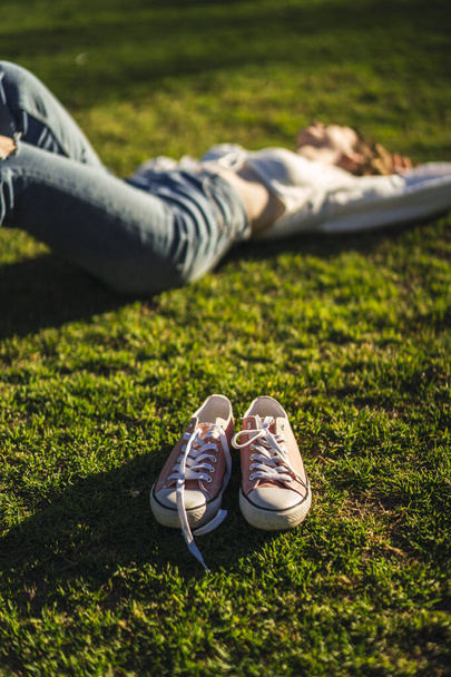 A vertical shot of pink shoes next to a beautiful Caucasian woman lying on the grass - Фото, зображення