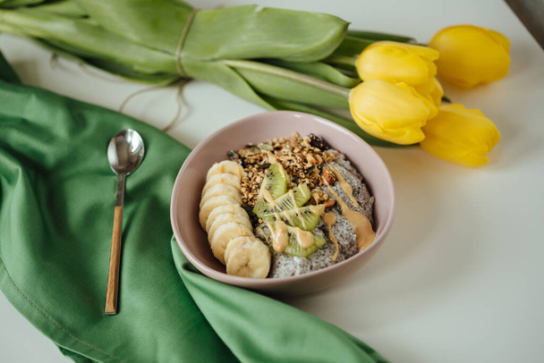 A top view shot of the healthy chia pudding on green cloth with yellow tulips. - Φωτογραφία, εικόνα