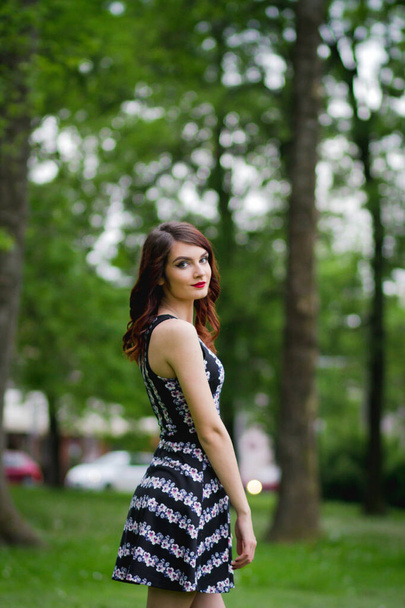 A beautiful Caucasian female with red lipstick posing in a park - Zdjęcie, obraz