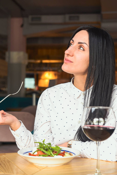 Young attractive woman having a healthy lunch in restaurant. Caucasian female with black hair dining. Eating out concept, eating alone in restaurant due to Covid-19 pandemic. - Foto, afbeelding