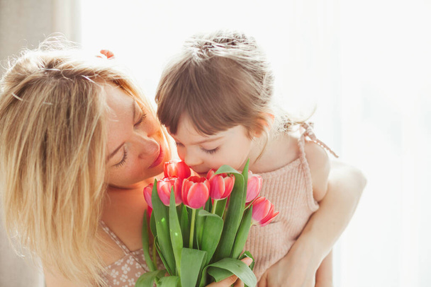A kislány és az anyja tulipánokat ölelgetnek és szaglásznak. Boldog anyák napját!! - Fotó, kép