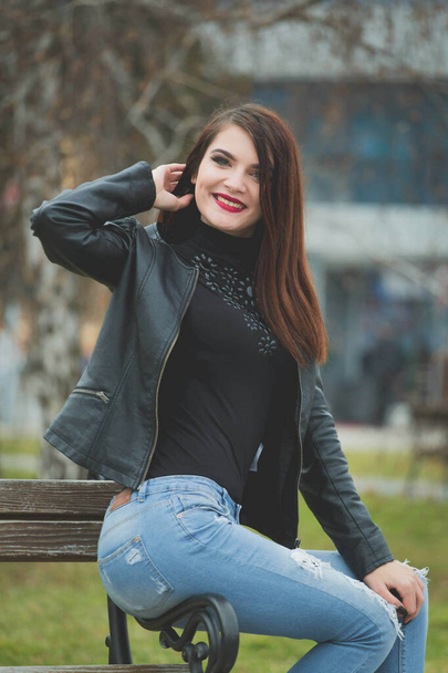 A beautiful Caucasian female with red lipstick and leather coat posing in a park - Foto, Bild