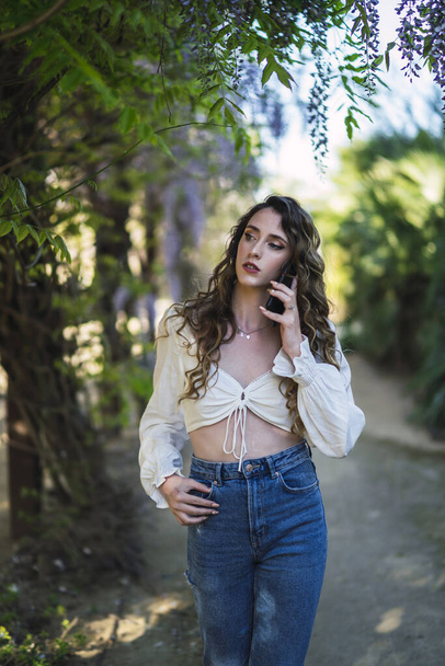 A vertical shot of a Caucasian woman from Spain talking on the phone in a park - Foto, immagini