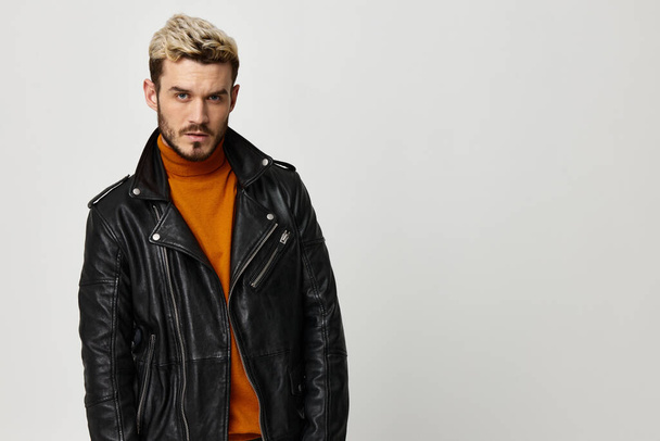 young man in leather jacket blond orange sweater light background - Photo, Image