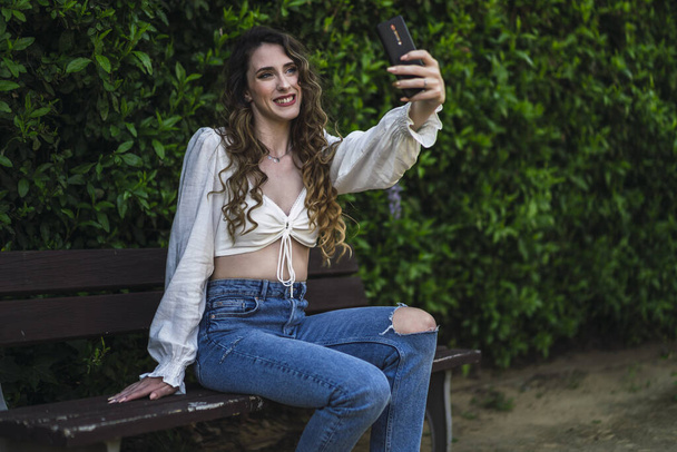 A shallow focus shot of a beautiful Spanish Caucasian woman wearing top and jeans, taking a selfie - Φωτογραφία, εικόνα