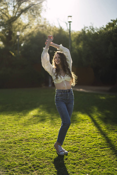 A vertical shot of a beautiful Spanish Caucasian woman wearing top and jeans, posing on the grass - Fotoğraf, Görsel