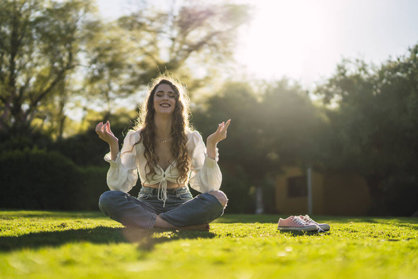 A shallow focus shot of a beautiful Spanish Caucasian woman with curly hair, meditating on the grass and smiling - Foto, Imagem