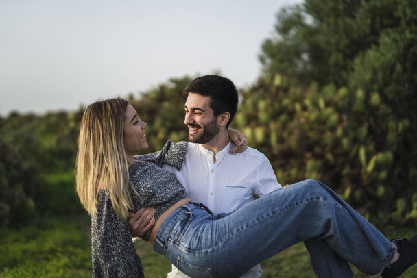 Une mise au point peu profonde d'un jeune homme portant sa petite amie dans ses bras dans un parc en Espagne - Photo, image