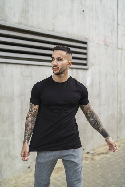 A vertical shot of a sexy tattooed male in a street style outfit posing outdoors - Foto, imagen