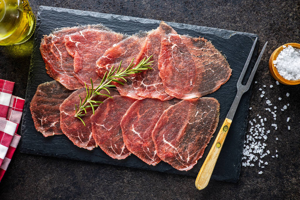 Sliced carpaccio. Raw beef meat on black cutting board. Top view. - Фото, изображение