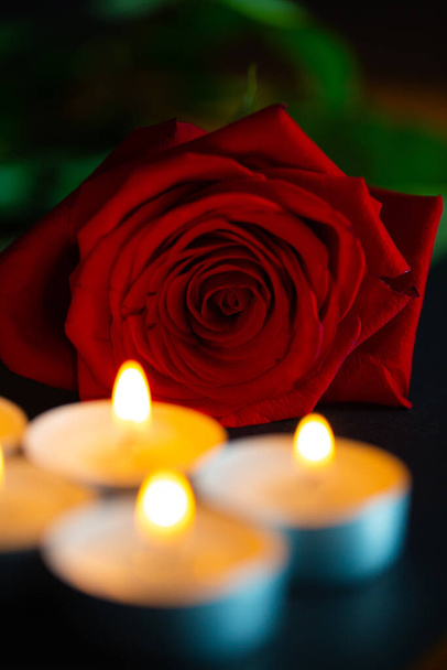 rode roos met kaarsen, zwarte achtergrond, rouw - Foto, afbeelding