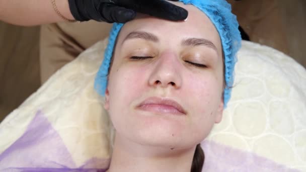 zbliżenie, kosmetyk w rękawiczkach medycznych stosuje równomiernie krem kosmetyczny lub krem przeciwsłoneczny do twarzy kobiet po złuszczaniu. pielęgnacja skóry i ochrona przeciwsłoneczna. kosmetologia na salon kosmetyczny - Materiał filmowy, wideo