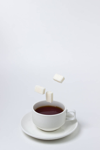 Sugar cubes fall into a cup of tea on a white background. A cup of tea with refined sugar. Tea time - Foto, Imagen