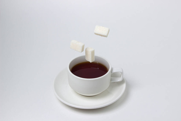 Sugar cubes fall into a cup of tea on a white background. A cup of tea with refined sugar. Tea time - Photo, image