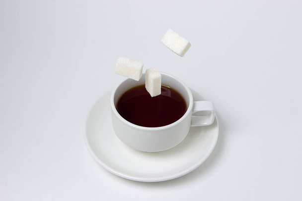 Sugar cubes fall into a cup of tea on a white background. A cup of tea with refined sugar. Tea time - Foto, imagen