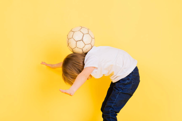 Aranyos fiú egy valódi bőrből készült labdával a kezében, sárga alapon. Foci - Fotó, kép