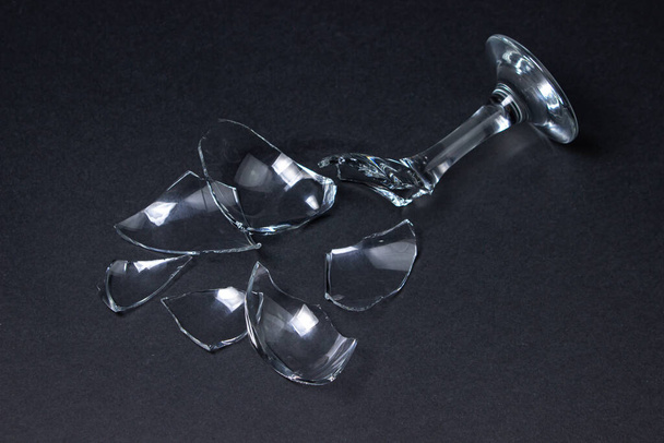 Broken wine glass on a dark background. Shards of a wine glass on a black background. Broken dishes - Foto, imagen