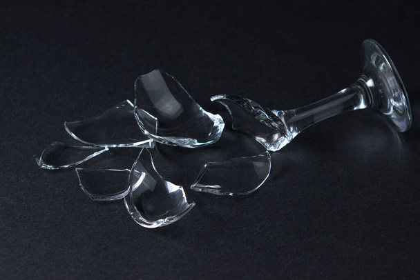 Broken wine glass on a dark background. Shards of a wine glass on a black background. Broken dishes - Photo, Image