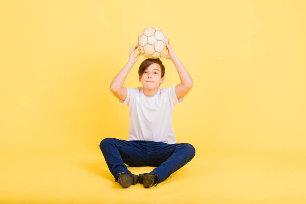 Милий хлопчик тримає футбольний м'яч з натуральної шкіри ізольовано на жовтому тлі. Футбол
 - Фото, зображення