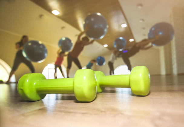 Malé zelené činky na dřevěné podlaze. Fitness převody v tělocvičně s dívkami dělat cvičení s míčky na pozadí. Sportovní a zdravý životní styl. Ženy začínají být fit. - Fotografie, Obrázek