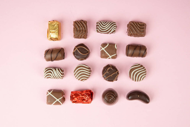 πάνω άποψη των διαφόρων πραλίνες σοκολάτα σε ροζ φόντο. Συλλογή σοκολατάκια καραμέλα. Ποικιλία σοκολάτες σε ροζ - Φωτογραφία, εικόνα