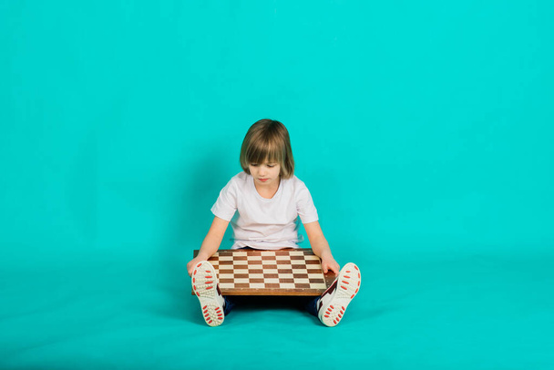 Χαριτωμένο παιδί κρατώντας ένα παιχνίδι σκάκι στην αγκαλιά του, στούντιο πυροβόλησε - Φωτογραφία, εικόνα