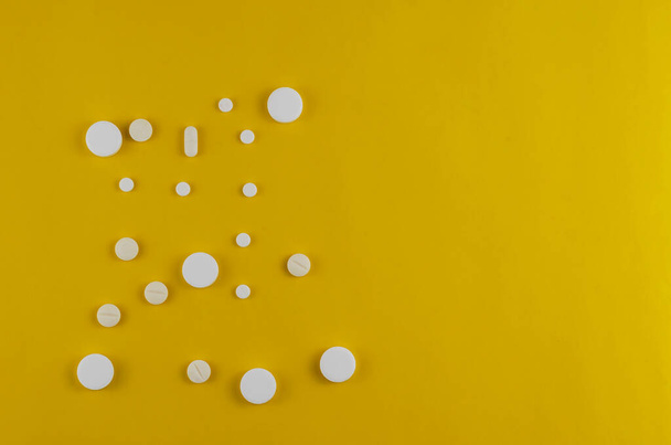 Μινιμαλιστική σύνθεση με τυχαία λευκά ιατρικά χάπια σε κίτρινο φόντο. Πάνω άποψη, επίπεδη lay. Αντιγραφή χώρου - Φωτογραφία, εικόνα