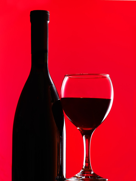 A bottle of red wine and filled with the same level of a wine glass on a red background - Fotografie, Obrázek
