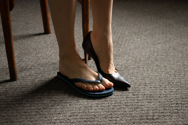un pied féminin en chaussures de plage et l'autre en chaussures à talons hauts noires sur le sol sur le robot, se reposer ou travailler - Photo, image