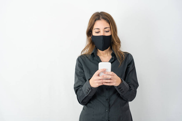 Studio shot of serious young model woman in business shirt clothes isolated on white copy space background looking at smartphone wearing medical protection mask. Stress for Covid-19 data news concept - Fotó, kép