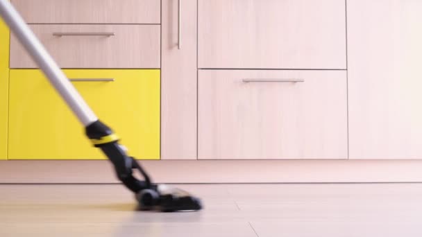 De rechtopstaande stofzuiger reinigt de laminaatvloer in de keuken. Vrouwenbenen. Grijze en gele tinten. Het concept van het schoonmaken van het huis, het schoon houden. - Video