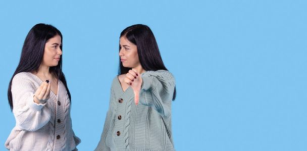 Banner, long format. Asking for explanation gestures. Twin sisters, confused women looking strange showing thumb down isolated on blue background with copy space for info ad text. High quality photo - Фото, изображение