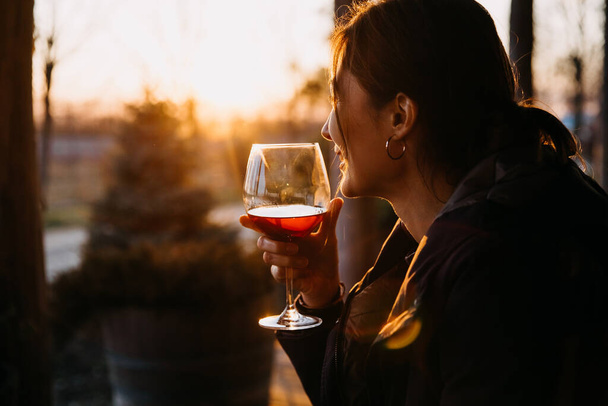 Молода жінка тримає стакан червоного вина під час заходу сонця, на відкритому повітрі
. - Фото, зображення