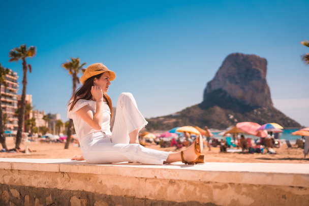 白い服を着た若い赤髪の白人の少女のライフスタイルとカルペ、バレンシアのビーチでわら帽子。スペイン - 写真・画像