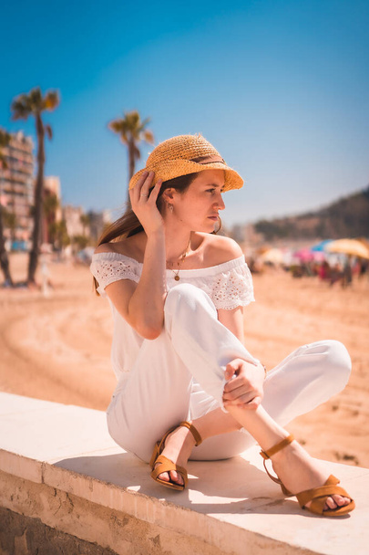 Lifestyle of a young red-haired Caucasian girl dressed in white and with a straw hat on the beaches of Calpe, Valencia. Spain. Enjoying the Mediterranean Sea - Zdjęcie, obraz