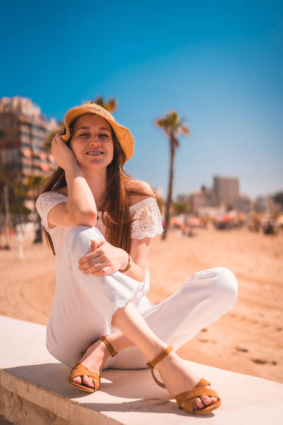 A Caucasian redhead dressed in white and with a straw hat on the beaches of Calpe, Valencia. Spain. Enjoying the summer in the Mediterranean Sea - Zdjęcie, obraz