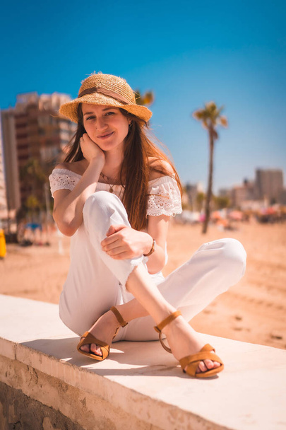 A Caucasian redhead dressed in white and with a straw hat on the beaches of Calpe, Valencia. Spain. Enjoying the Mediterranean Sea - Valokuva, kuva