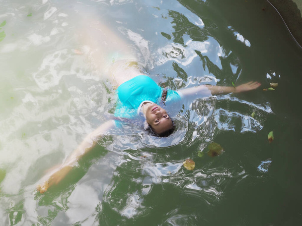 Een meisje in een blauwe top zwemt in modderig water met haar armen uitgestrekt naar de zijkanten - Foto, afbeelding
