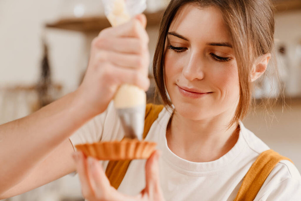 Красива задоволена випічка шеф-кухаря жінка робить пиріг з вершками на затишній кухні
 - Фото, зображення