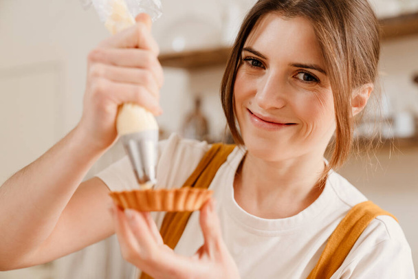 Beautiful happy pastry chef woman smiling while making tart with cream at cozy kitchen - Valokuva, kuva
