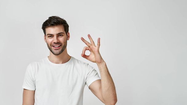 Young man in white t-shirt showing okay gesture - Φωτογραφία, εικόνα