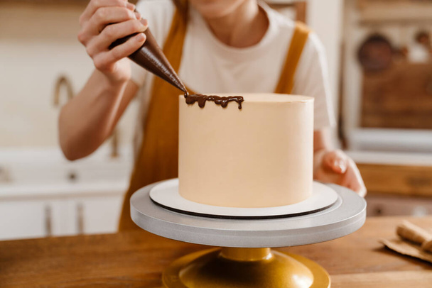 Καυκάσια σεφ ζαχαροπλαστικής γυναίκα κάνει κέικ με κρέμα σοκολάτας σε εσωτερικούς χώρους - Φωτογραφία, εικόνα