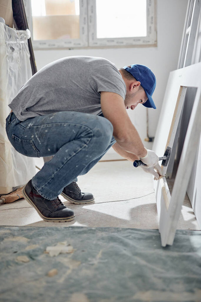 Jonge volwassen man werkt aan een DIY budget renovatie van zijn nieuwe woning. - Foto, afbeelding