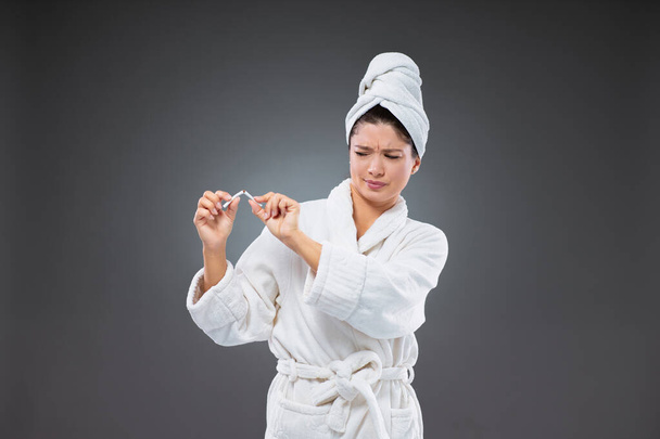 Una mujer adulta con una bata de baño y una toalla envuelta alrededor de su cabeza rompe un cigarrillo por la mitad y se convierte en hábitos saludables. Di no al vicio - Foto, imagen