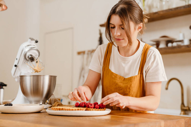 Beautiful concentrated pastry chef woman making tarts with berries at cozy kitchen - Zdjęcie, obraz