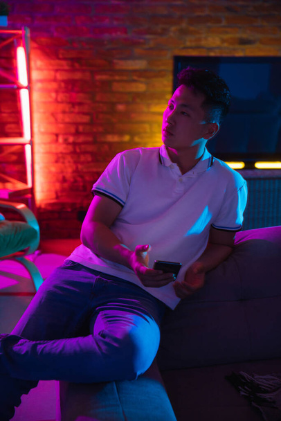 Portrait of young Korean man isolated at home interior in gradient blue neon light - Photo, Image
