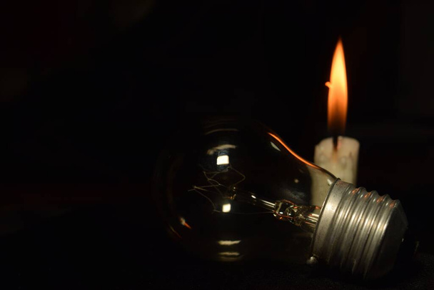 una lampada e una candela sfocano bruciando sullo sfondo scuro, durante un'interruzione di corrente. inizio blackout. - Foto, immagini