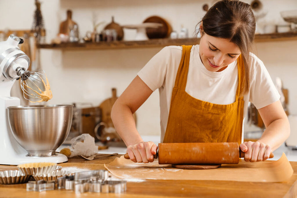 Caucasian focused pastry chef woman making dough with rolling pin at cozy kitchen - Foto, imagen