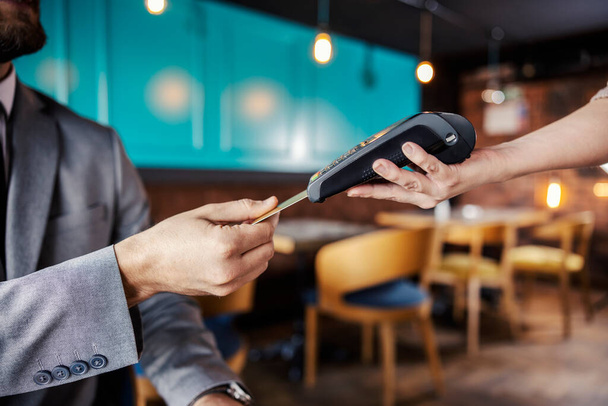 Hands holding a payment terminal. A man elegantly dressed in a business suit puts a credit or debit card in an online payment terminal held by a feminine hand. Paying bills for a meal at a restaurant - Photo, Image